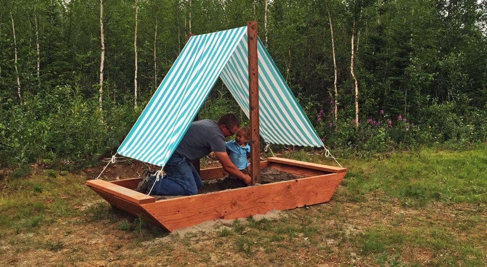 Boat-shaped wooden sandbox with a real cloth sail and mast