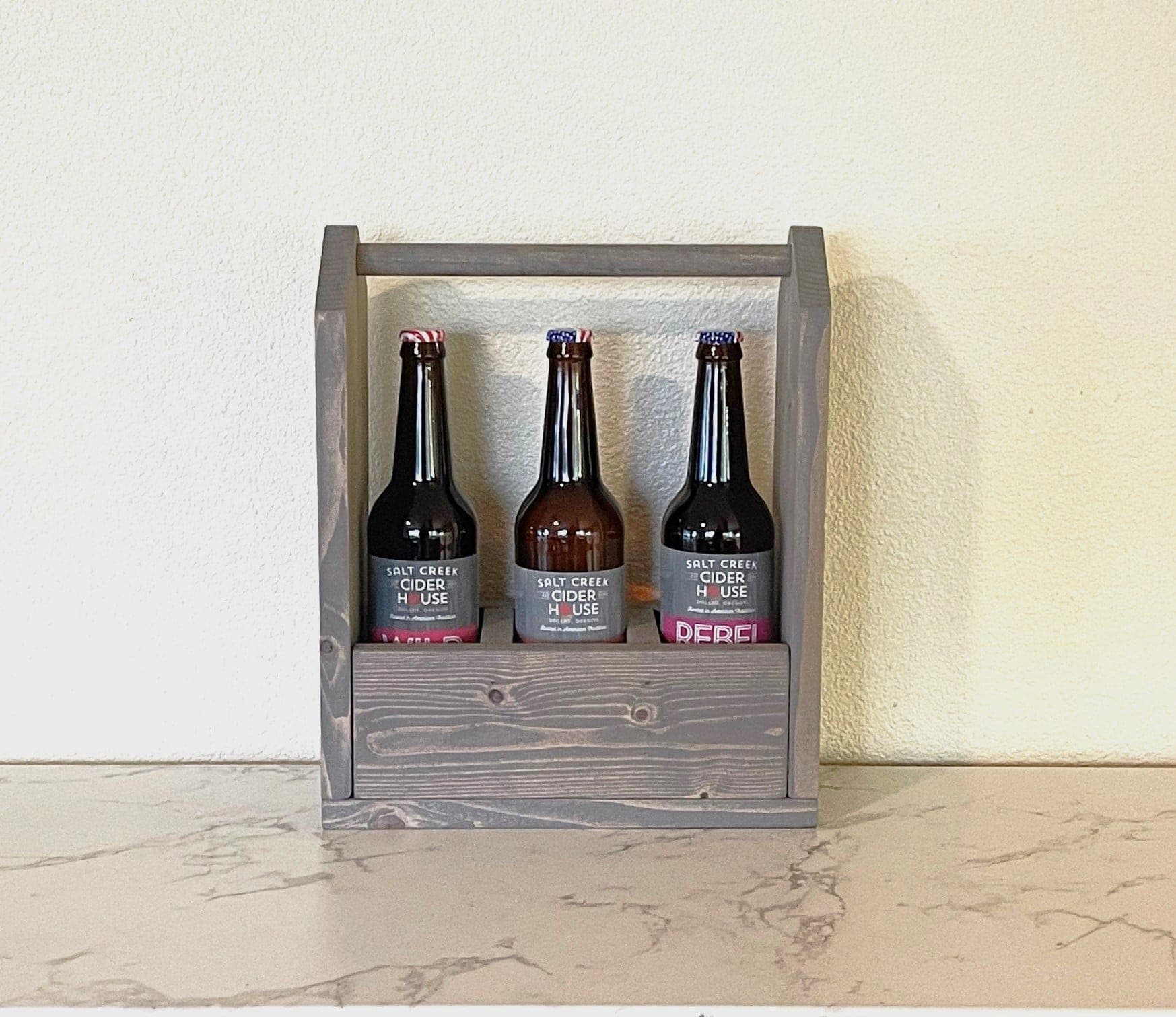 A small wood bottle caddy with a dowel handle carrying three bottles