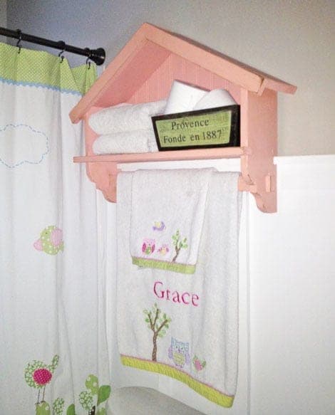 Wall-mounted bathroom shelf with a birdhouse-style peaked roof and a built-in wooden towel bar