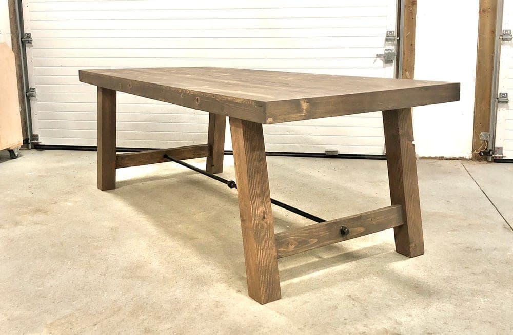 A farmhouse dining table with splayed 4x4 legs joined by an iron pipe stretcher
