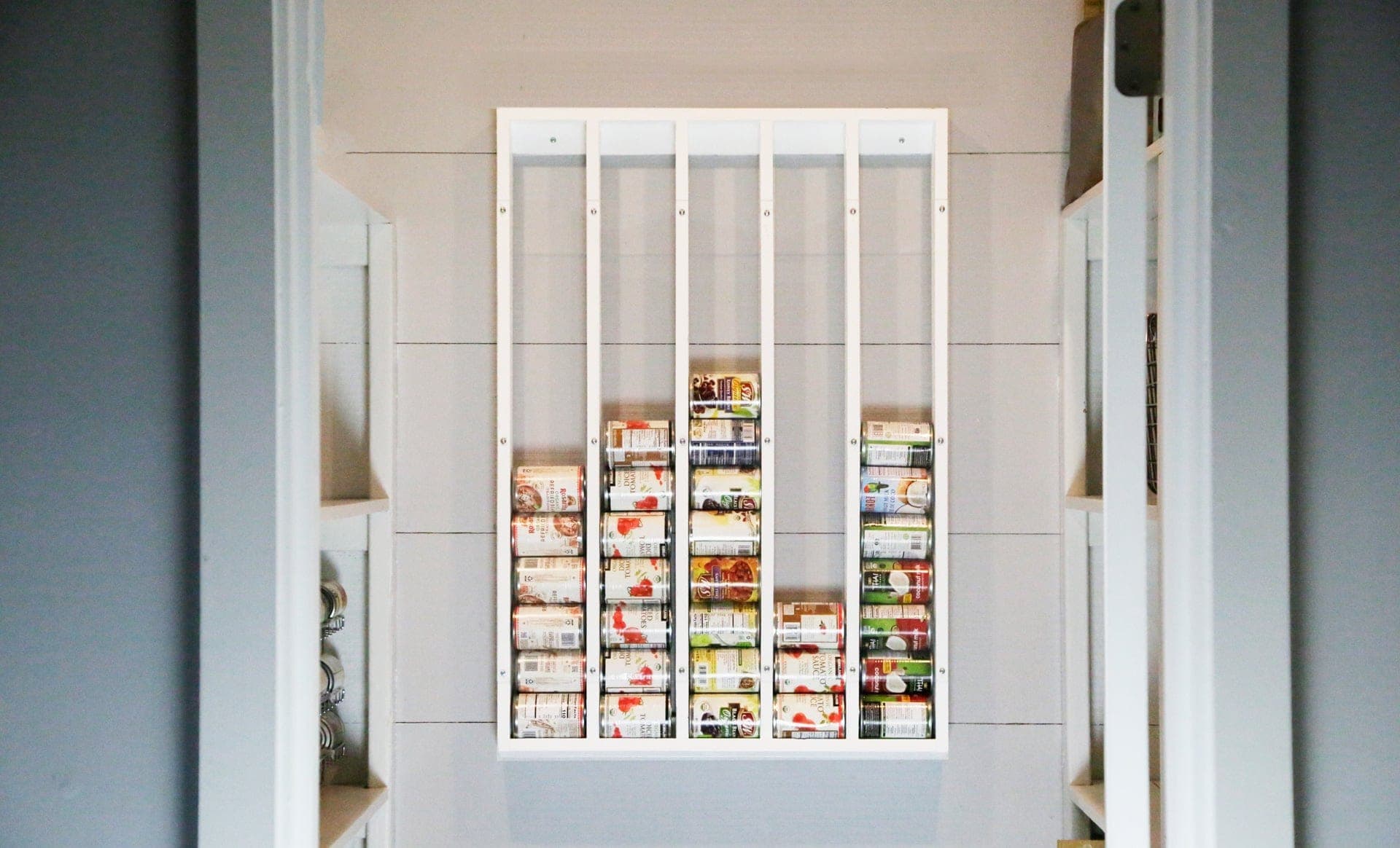 Wall-mounted gravity-fed can organizer with sloped lanes and acrylic face