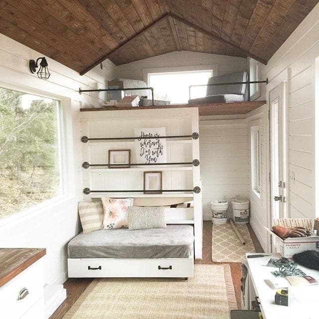 A built-in tiny-house loft with a queen bed over storage drawers and a shelf wall