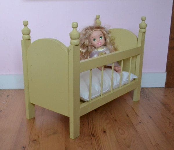 Small fancy doll crib with dowel-railed sides and finial-capped end posts