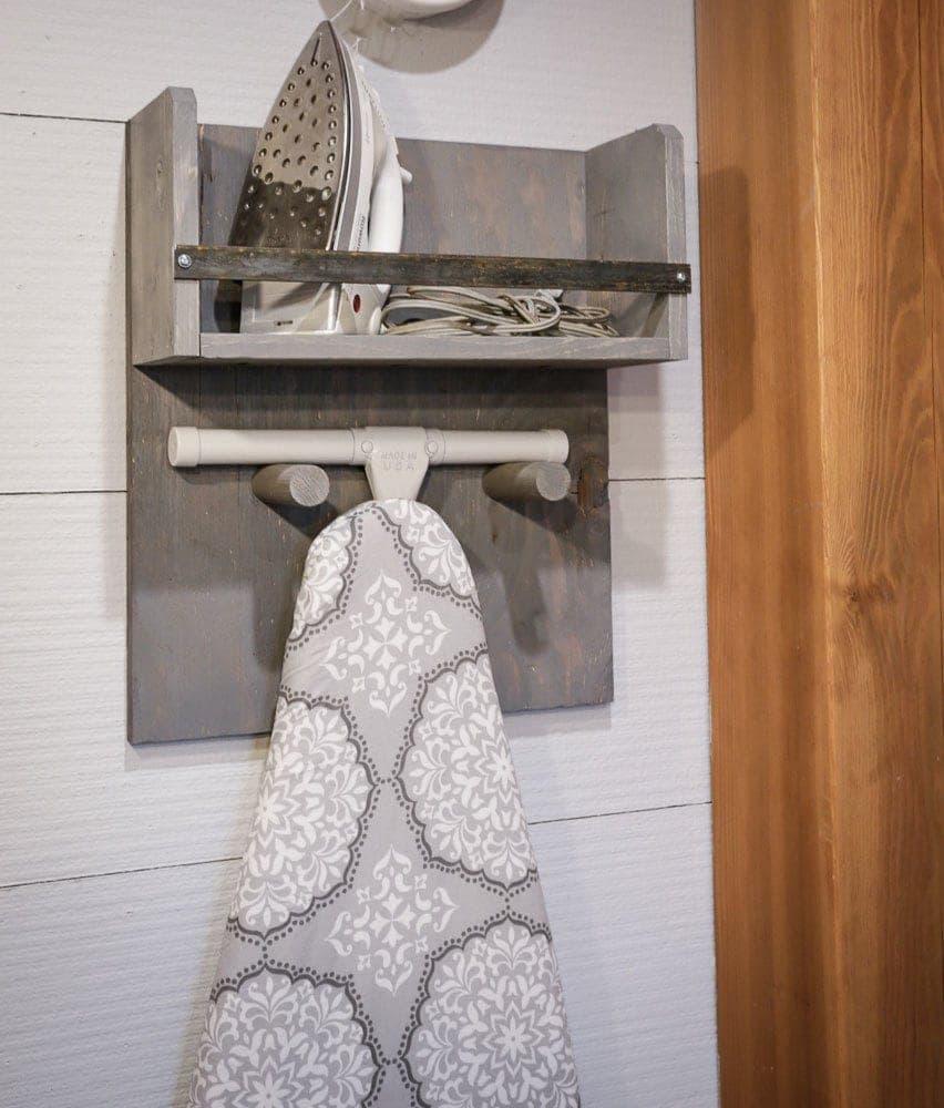 Wall-mounted wooden holder for an ironing board with dowel pegs and an iron bar
