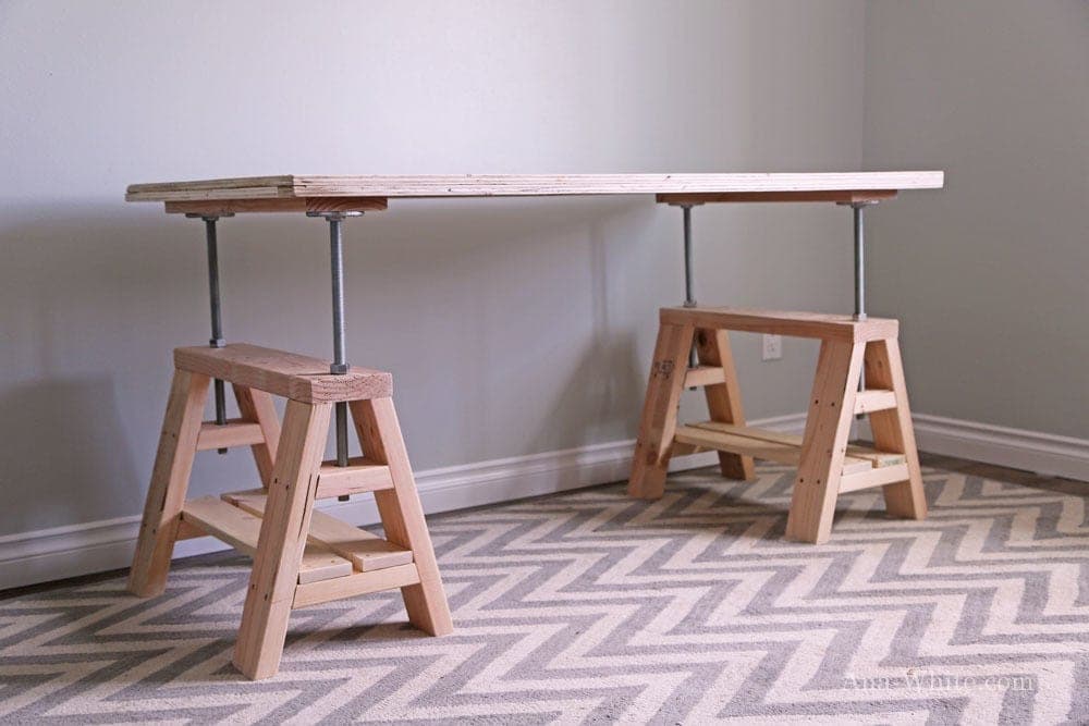 Industrial adjustable-height desk with angled sawhorse legs on threaded rod