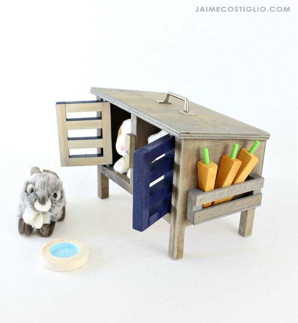 Small wooden toy bunny hutch with barred doors and a sloped roof