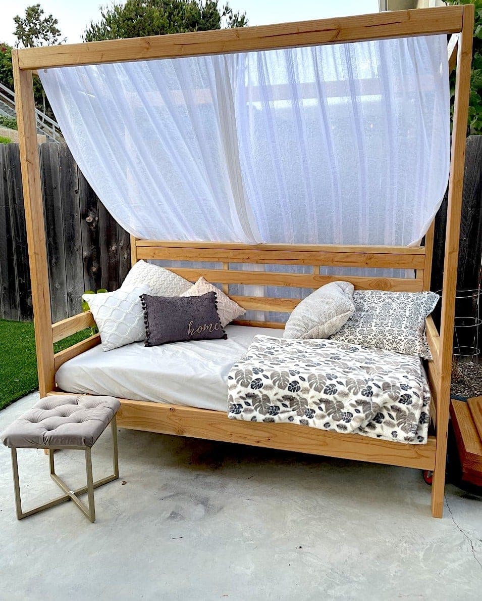 Raised outdoor daybed on tall corner posts with a slatted privacy back