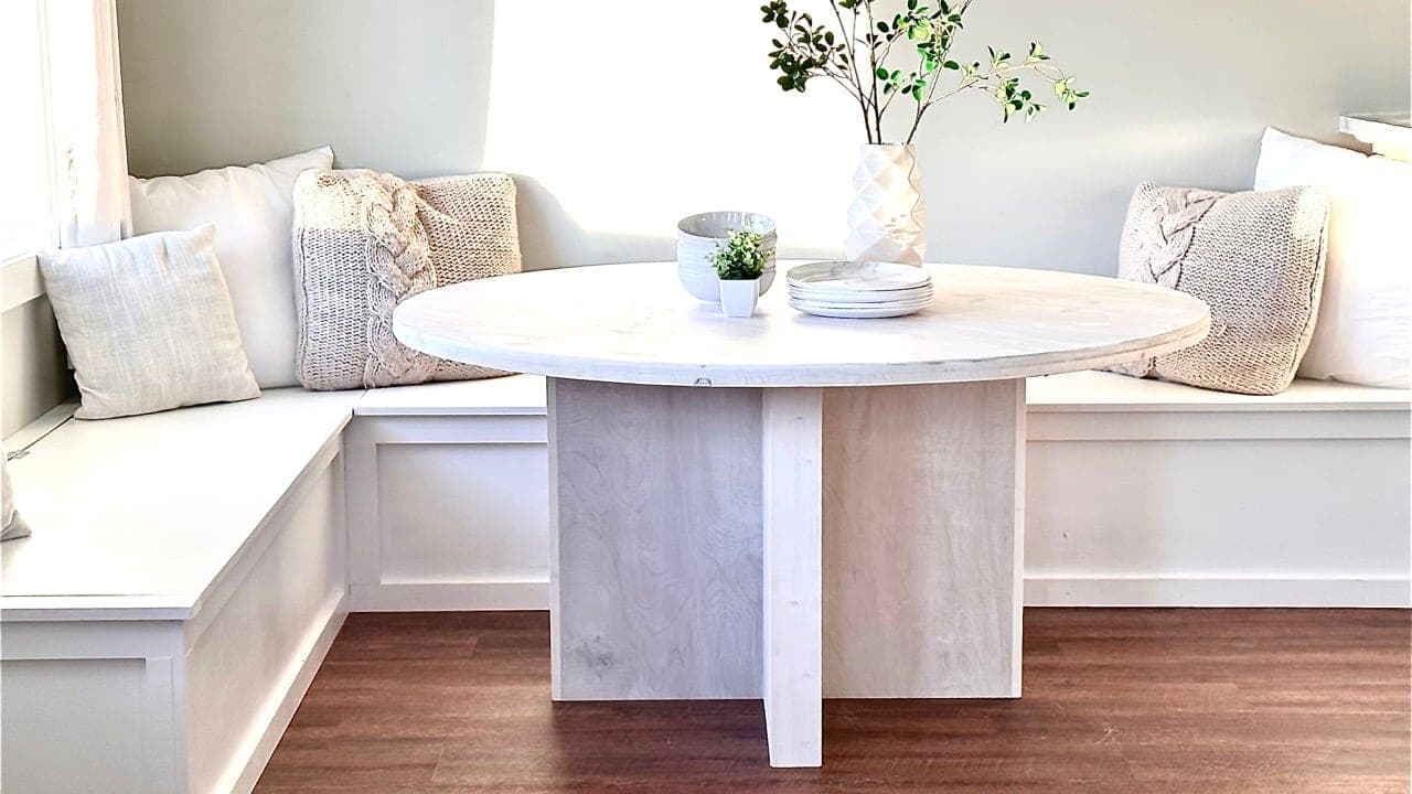 A minimalist plywood pedestal base supporting a round dining tabletop