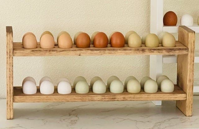 A wooden countertop egg holder with two drilled shelves displaying a dozen eggs