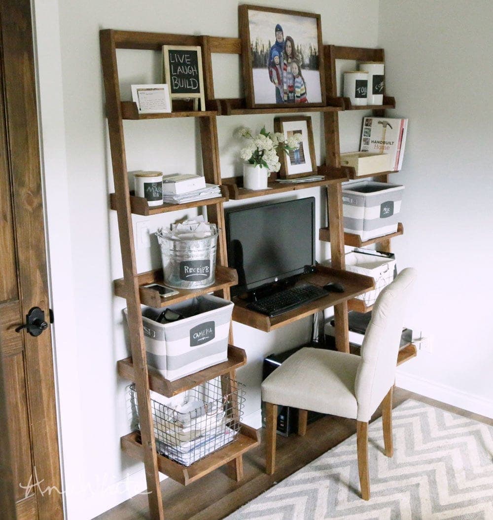 Leaning ladder desk with a writing surface and graduated shelves against a wall