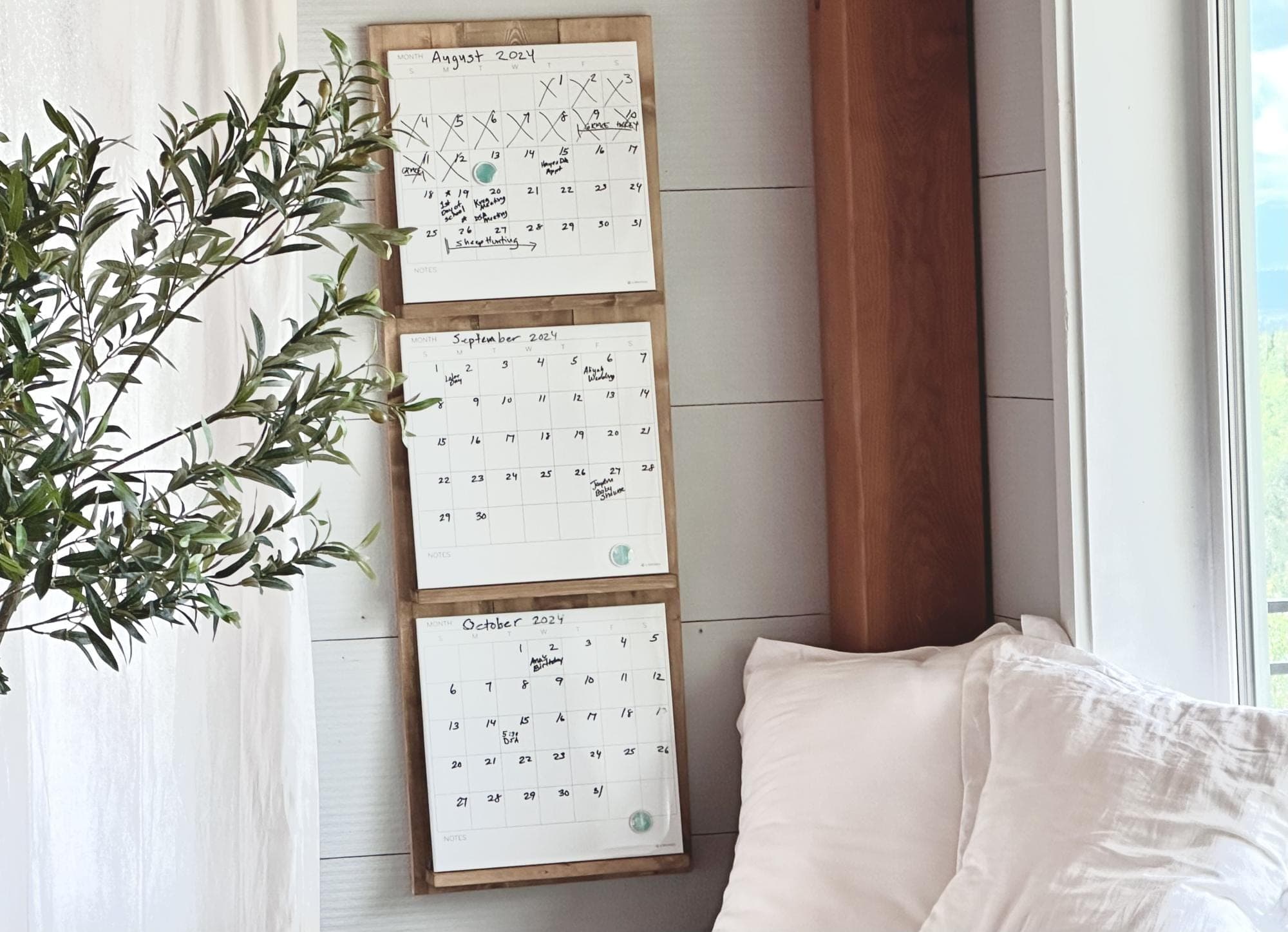 A wall-mounted shelf holding three dry-erase calendar panels side by side