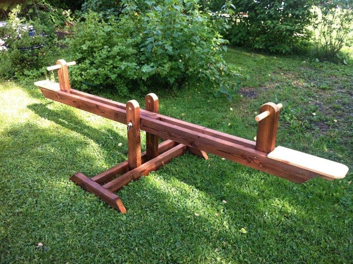 Backyard wooden seesaw with padded seats and dowel handles on a cross base