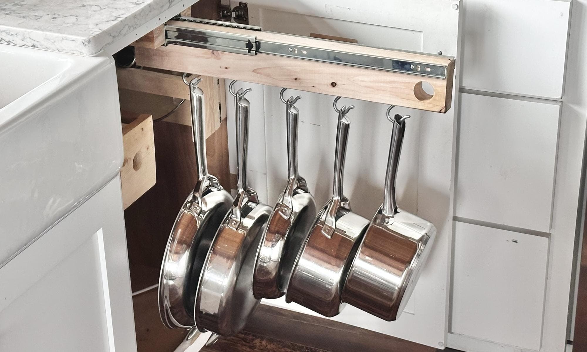 Pull-out pot rack with pans hanging from hooks, extended from a base cabinet