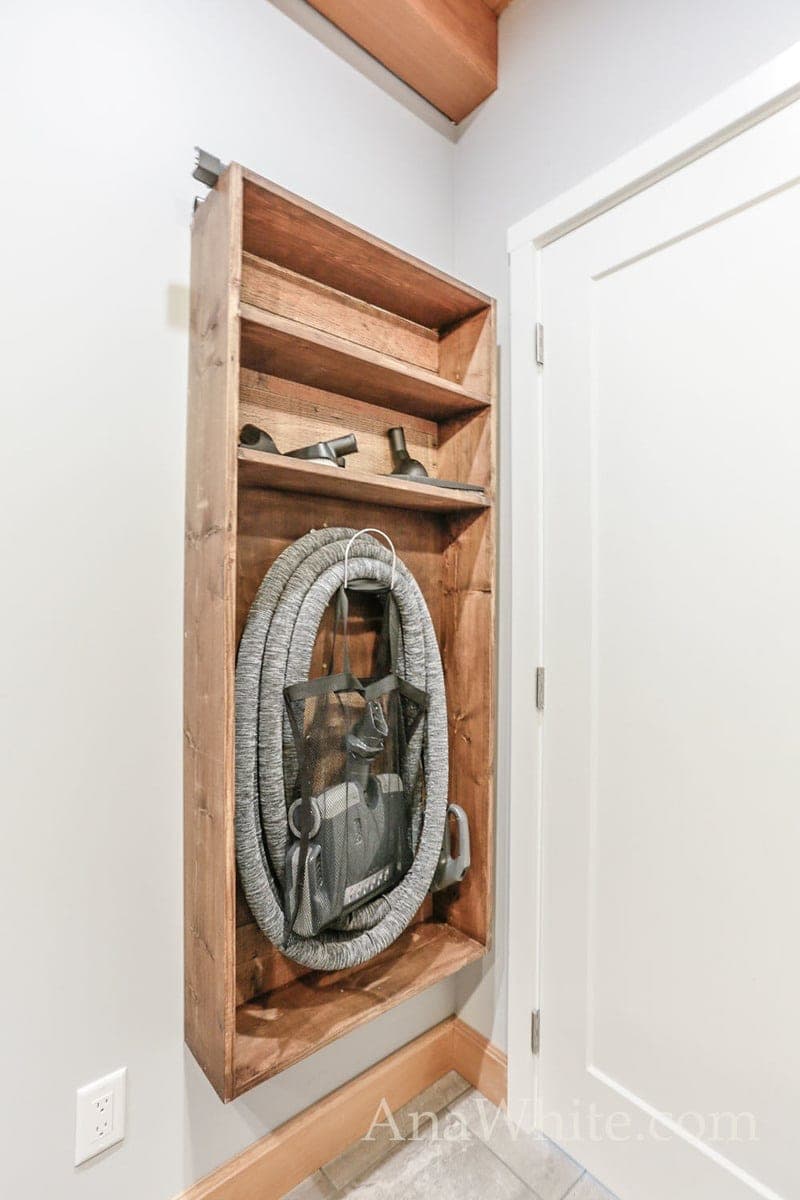 Wall-mounted shelf organizer holding a central vac hose reel